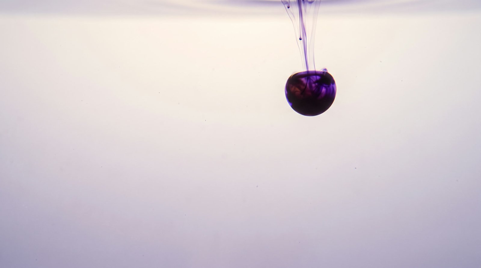 A single drop of violet ink entering still, pale water